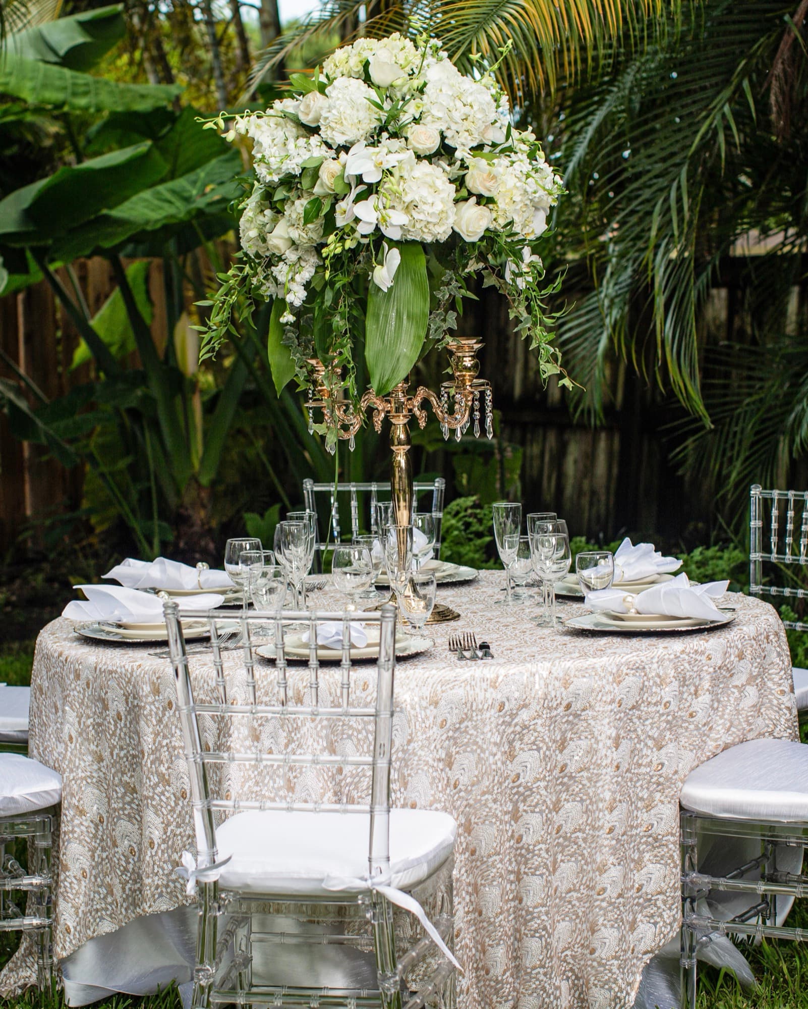 Outdoor round table with a lace overlay, crystal chairs and a tall white floral candelabra centerpiece