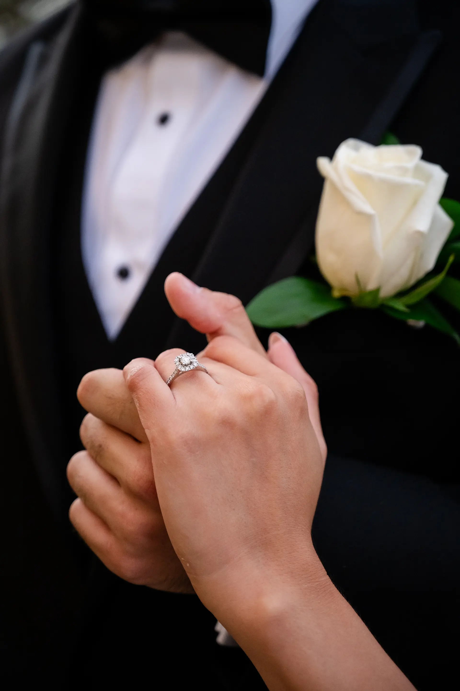 Bride and groom holding hands, ring and rose boutonnière in focus